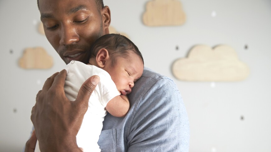 A man holds his infant child while in a home nursery